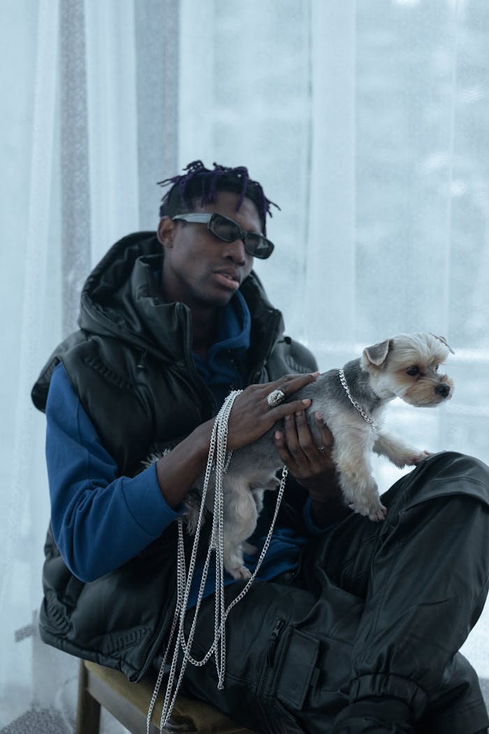 Man with sunglasses holds a Chihuahua indoors, showcasing modern urban fashion.